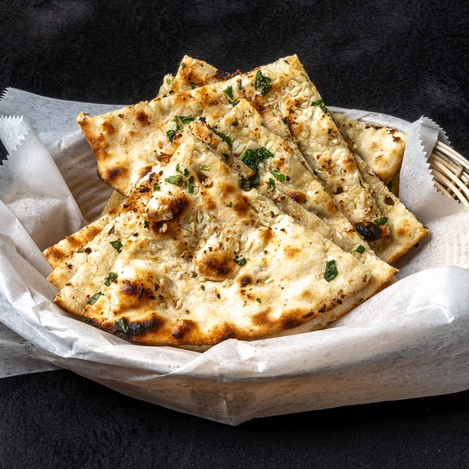 Anjappar Chettinad Indian Restaurant's garlic naan bread, garnished with herbs, served in a basket.