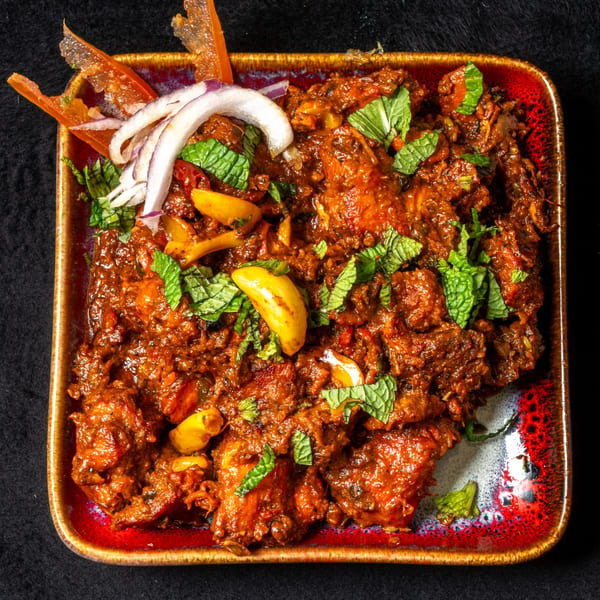 Anjappar Chettinad Indian Restaurant's spicy chicken curry, garnished with mint, garlic, and sliced red onions.