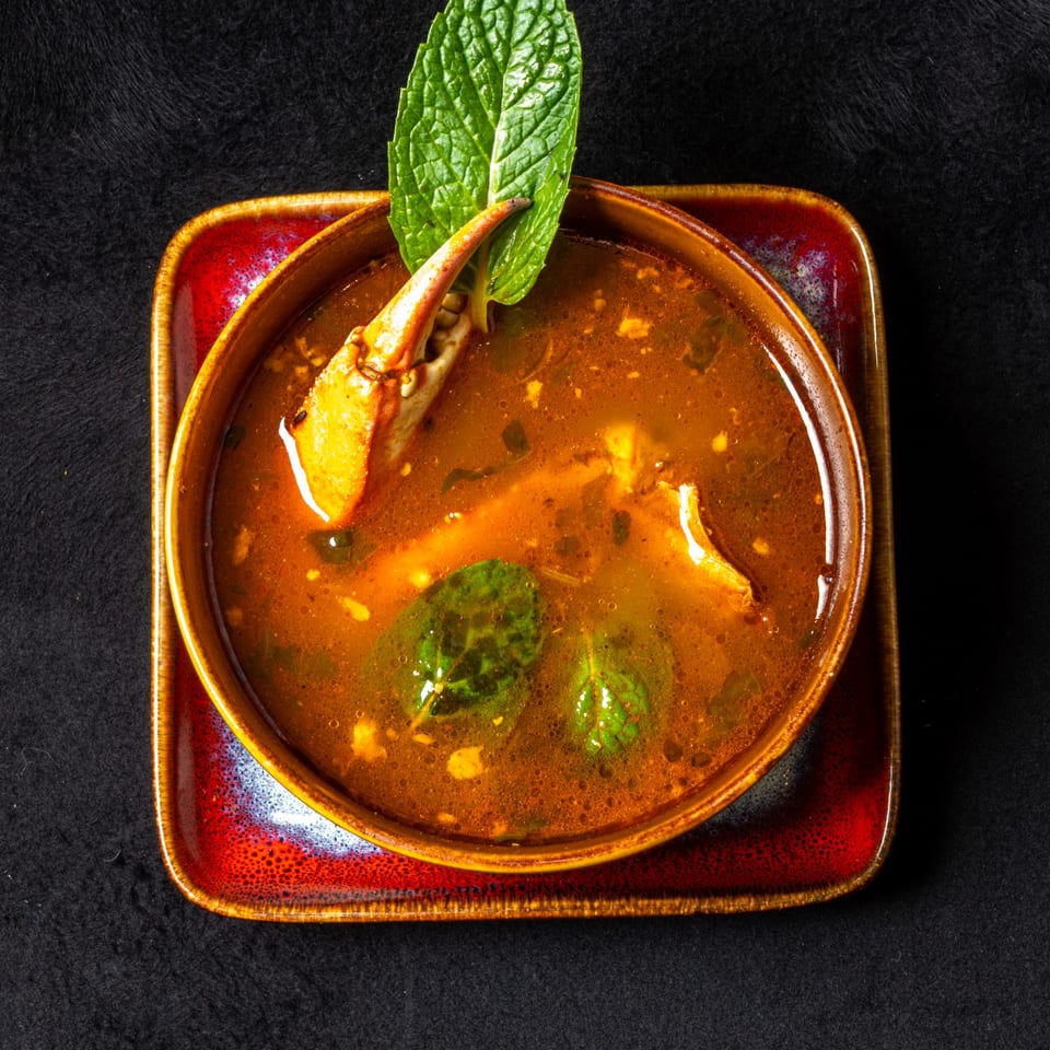 Anjappar Chettinad Indian Restaurant's crab soup with a crab claw and mint leaf garnish.