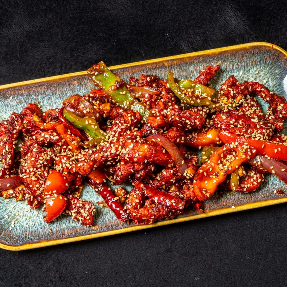 Anjappar Chettinad Indian Restaurant's chili chicken, a vibrant red dish with bell peppers and sesame seeds.