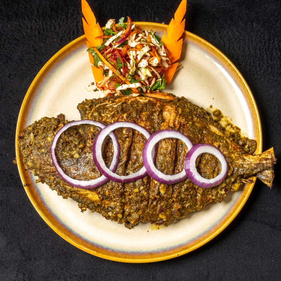 Whole grilled fish, coated in green Indian spices, garnished with red onion rings and a side salad.