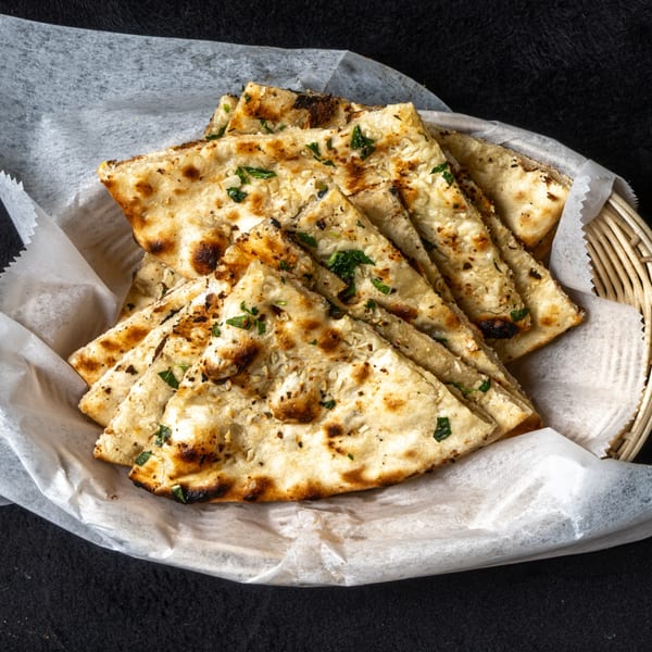 Indian garlic naan bread, cut into triangles, served in a basket lined with white paper.