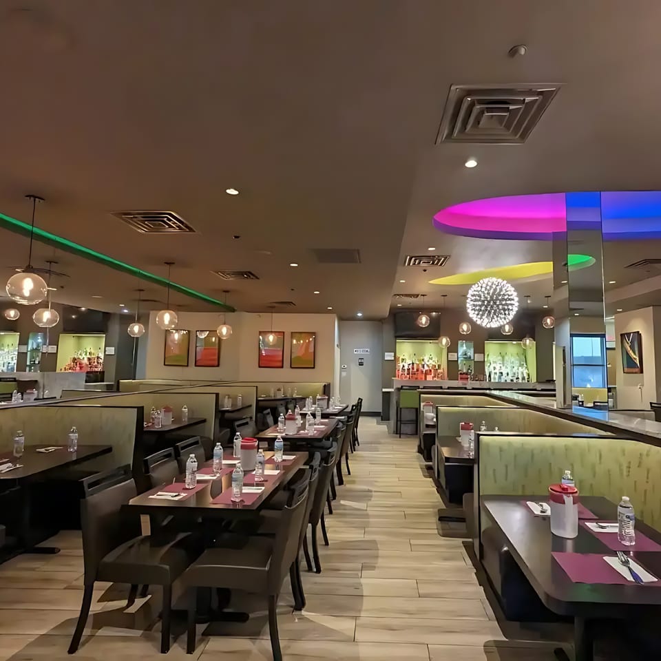 Anjappar Chettinad Indian Restaurant dining room with tables, booths, and a bar area with colorful lighting.