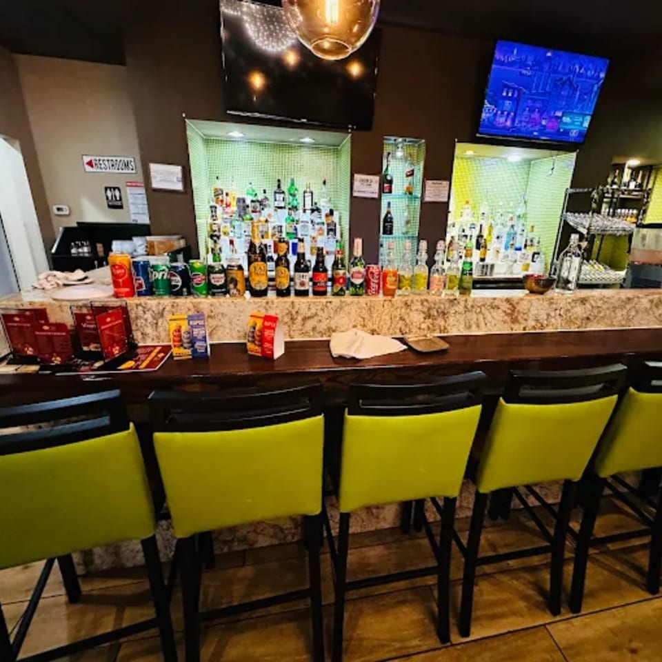 Anjappar Chettinad Indian Restaurant's bar area with a fully stocked liquor shelf and lime green bar stools.