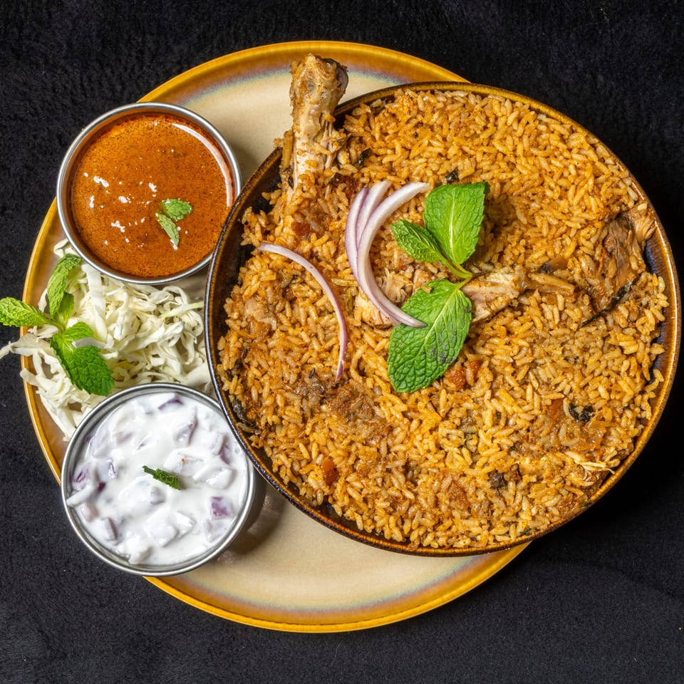 Anjappar Chettinad Indian Restaurant's chicken biryani with raita, gravy, and cabbage salad on a gold plate.