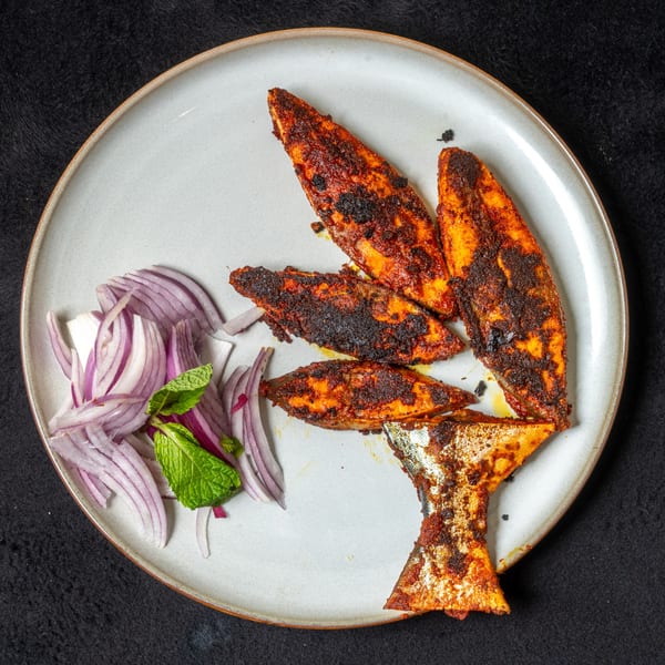 Anjappar Chettinad Indian Restaurant's spicy fried fish pieces with sliced red onions and mint on a plate.