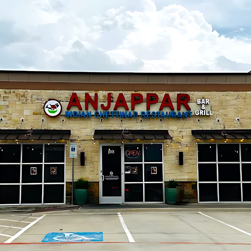 Exterior of Anjappar Chettinad Indian Restaurant with a stone facade and large windows.